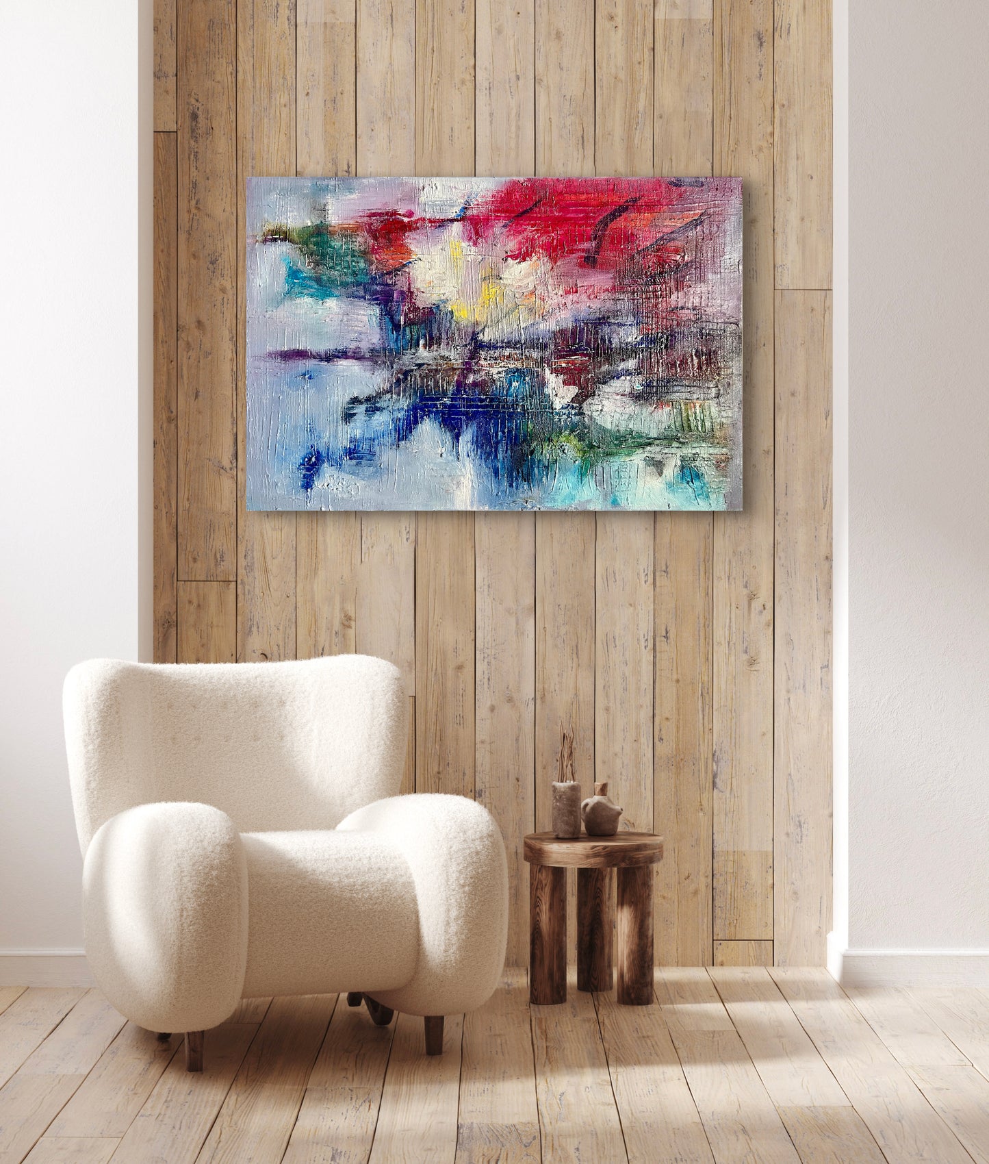 Reflection of Chaos, an oil and acrylic ink based abstract painting by Beatrice Morel, shown in a room setting with a chair, featuring fiery reds and oranges, which clash against deep blues and greens.
